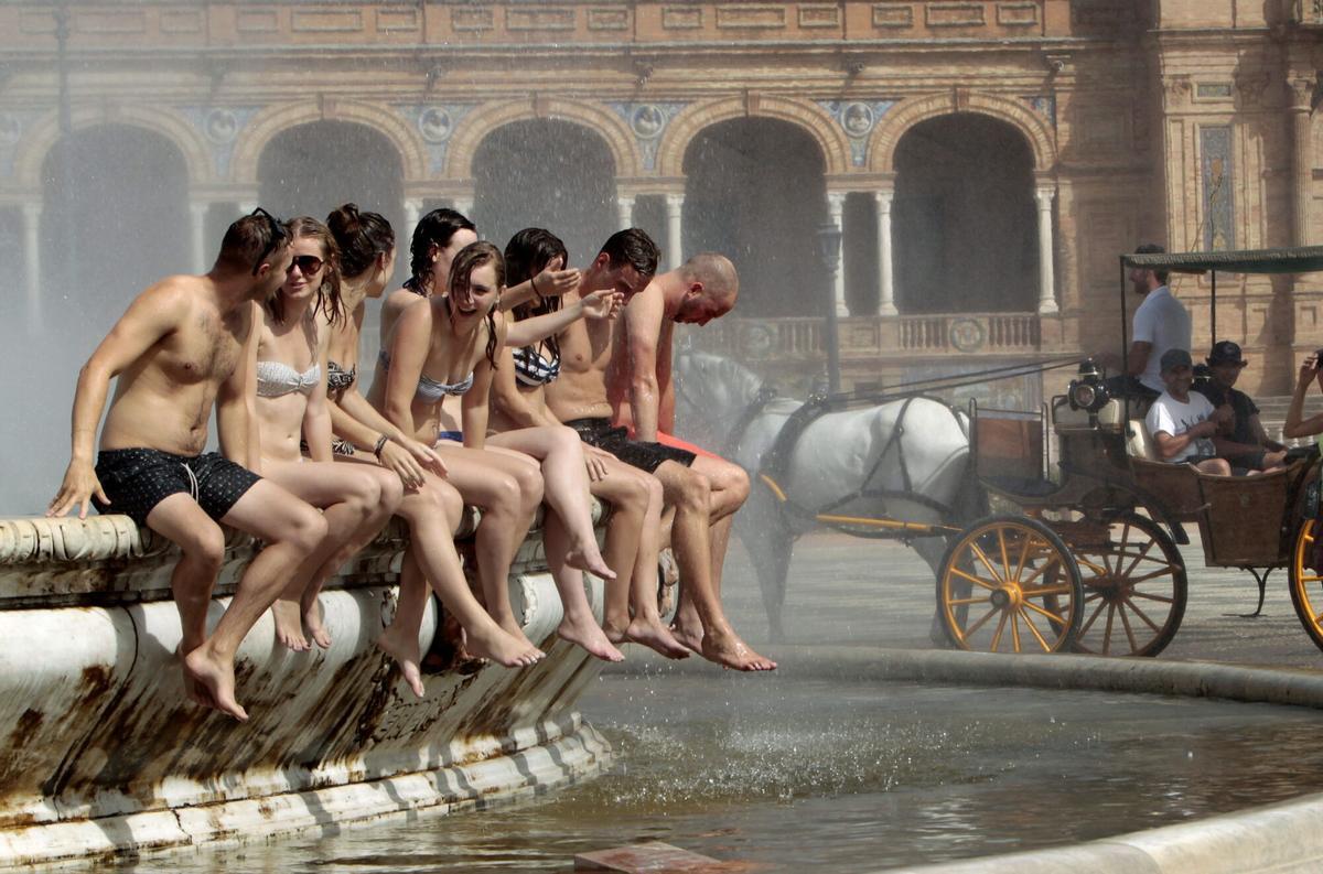 Un grupo de turistas extranjeros en bañador se refrescan en la fuente central de la sevillana Plaza de España
