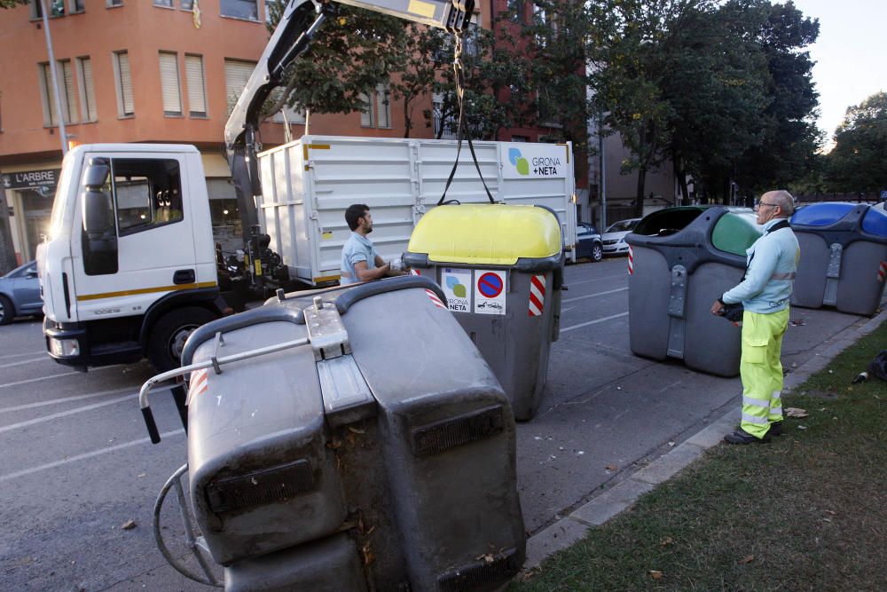 Carrers amb restes de mobiliari urbà cremat, contenidors per terra i treballadors de la brigada treballant