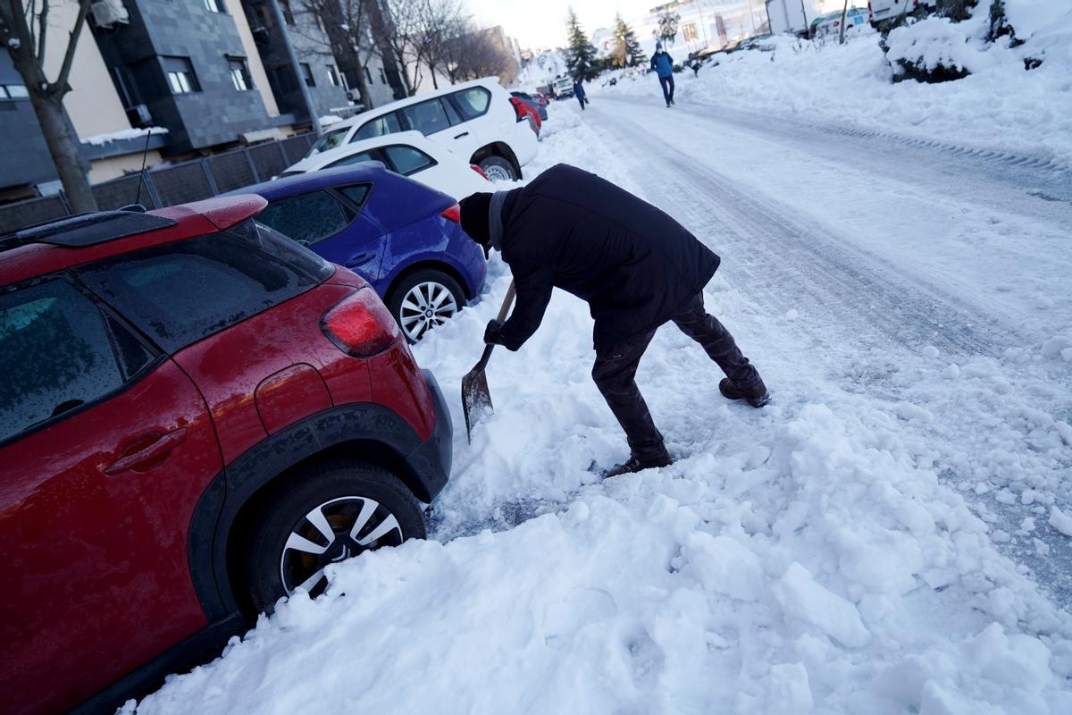 Una persona quita nieve para poder sacar el coche e ir a trabajar.