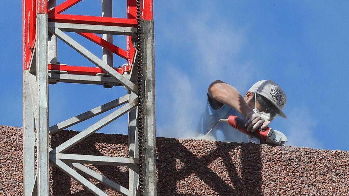 Un operario trabaja con una radial en el muro de un edificio de viviendas.