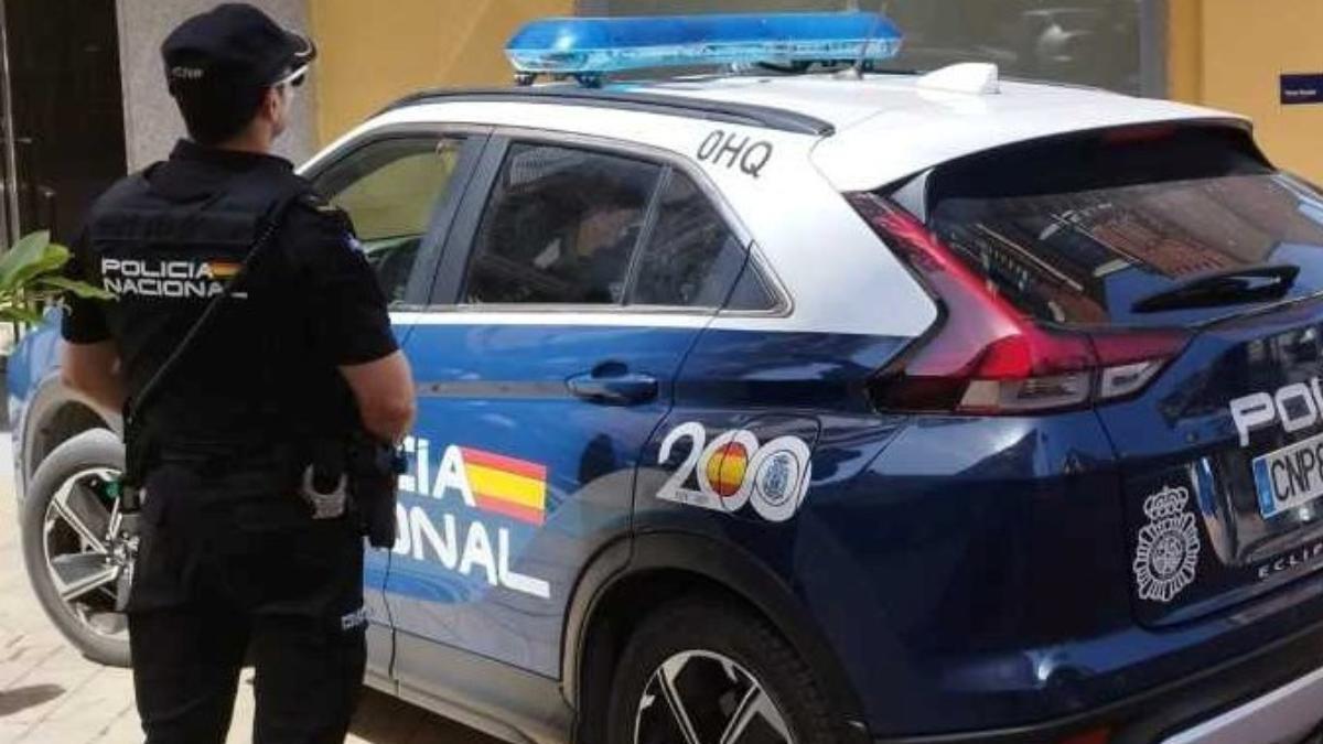 Imagen de un policía nacional junto al coche patrulla.