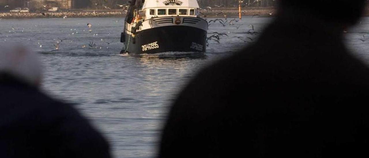 Dos hombres observan la llegada de un pesquero al puerto de Avilés.