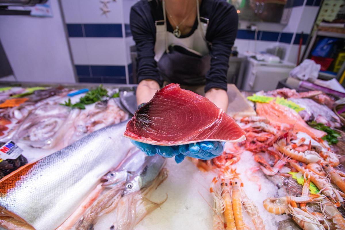 Una pescadera muestra un corte de atún desde su mostrador.