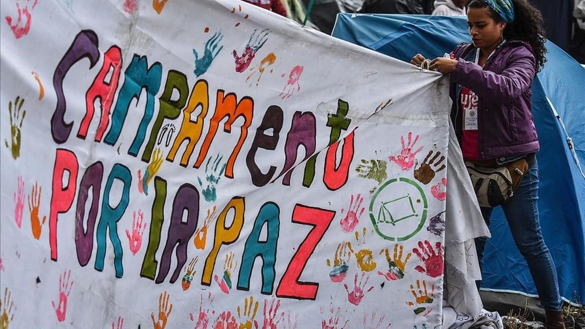 Una joven ayuda a colocar una pancarta a favor del acuerdo de paz en la acampada de la plaza Bolivar, en Bogotá.
