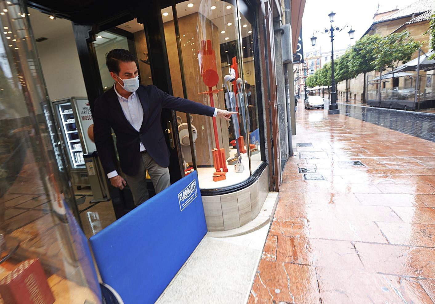 Francisco Gayoso, con la tabla que usó para contener la entrada del agua en su negocio de la calle San Francisco de Oviedo, ayer, señalando la zona, tranquila tras las inundaciones del miércoles. | Miki López