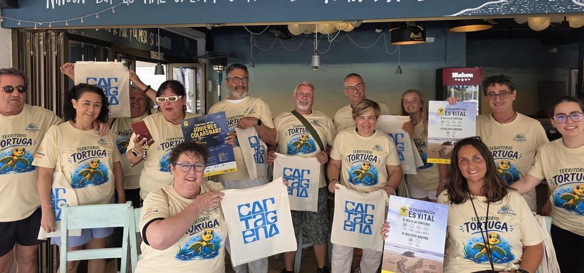 Los voluntarios de 'Territorio Tortuga' sostienen carteles y bolsas de la iniciativa.