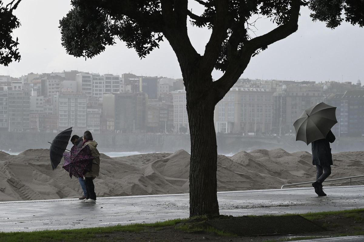 Viandantes se protegen de la lluvia en el paseo marítimo de A Coruña.