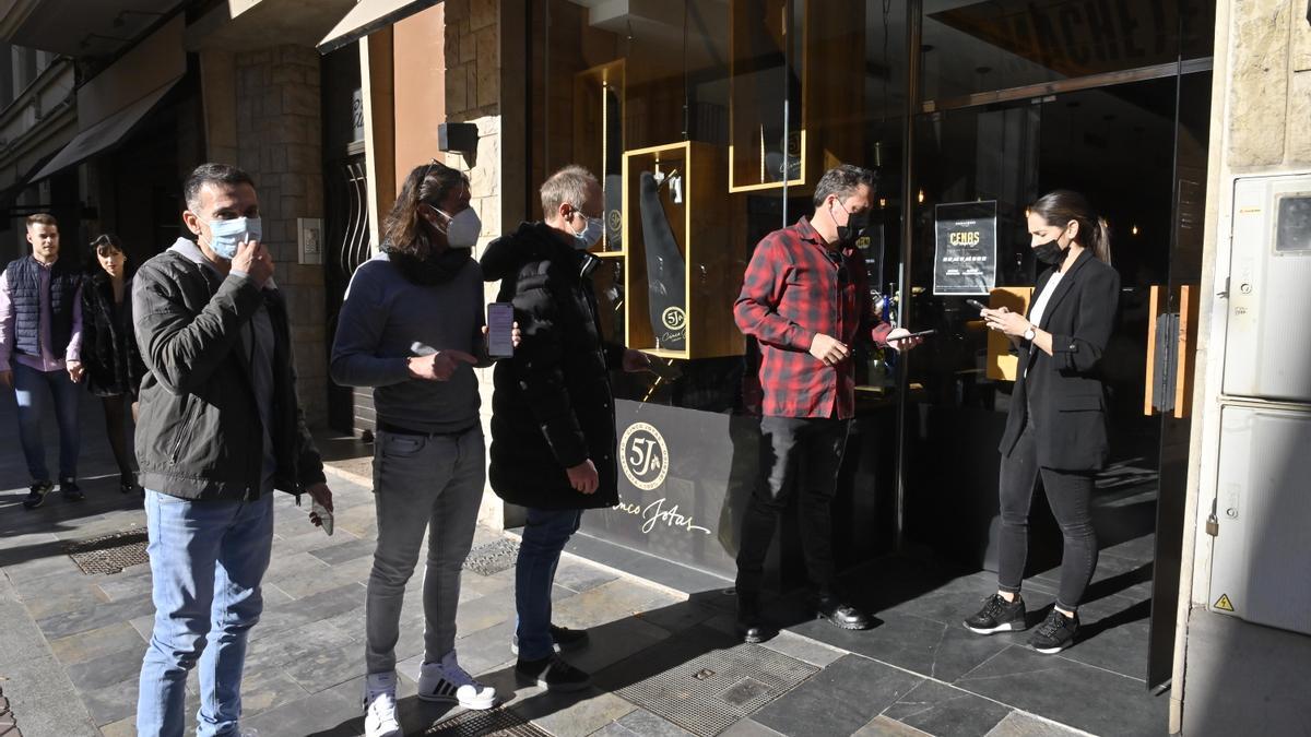 Un grupo muestra este sábado a mediodía a una empleada su certificado covid de vacunación en el acceso la Taberna Machete, en el centro de Castelló.