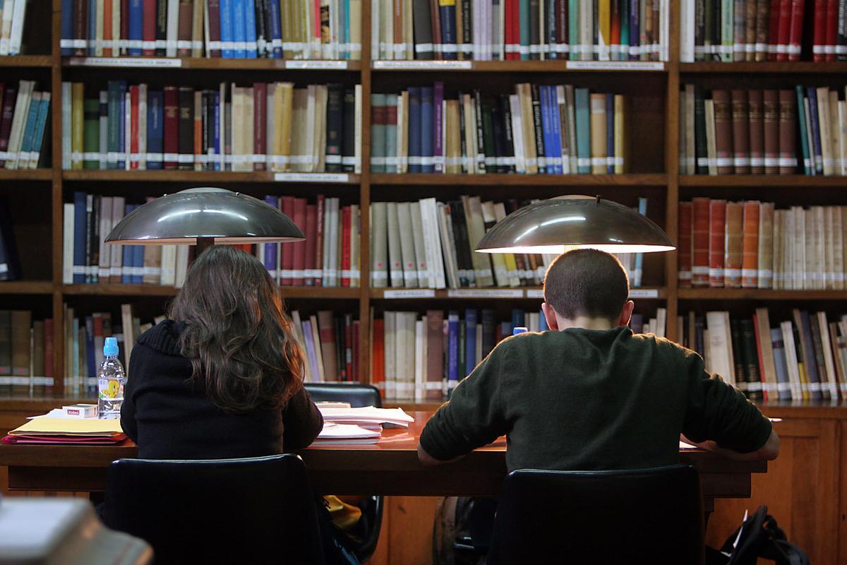 Dos estudiantes repasan sus apuntes en una biblioteca.