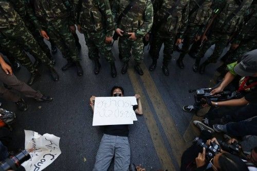 A man lies on the ground in front of police while holding a placard during a protest against martial law, in central Bangkok