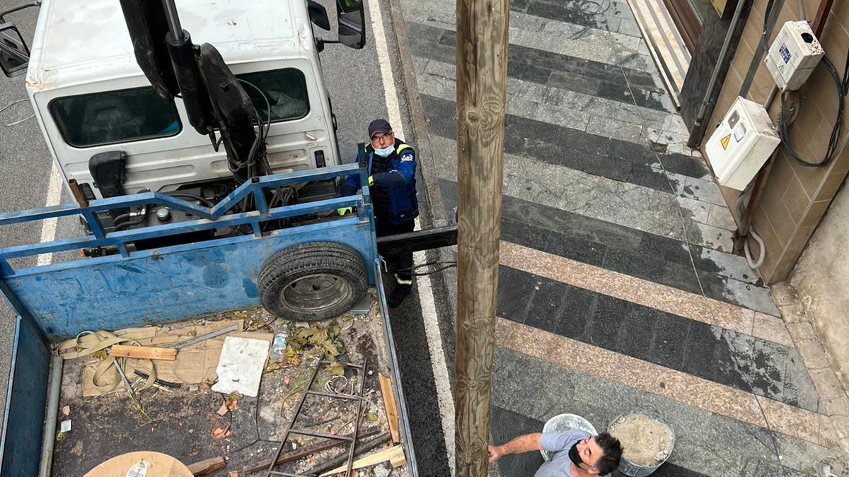 Operarios retirando, con ayuda de una grúa, uno de los postes de la calle Mayor.