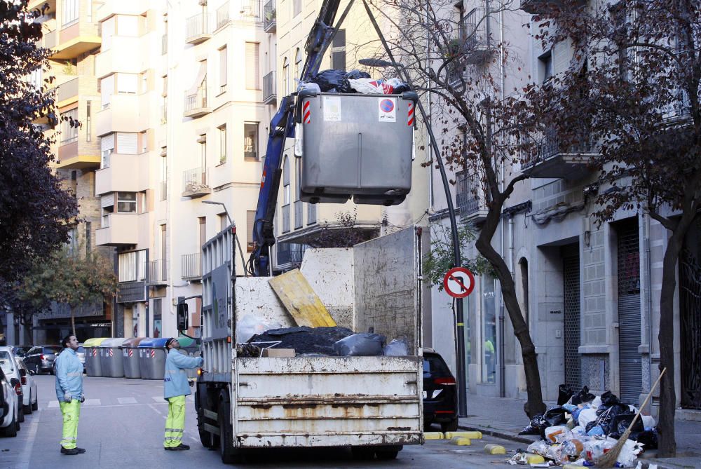 Carrers amb restes de mobiliari urbà cremat, contenidors per terra i treballadors de la brigada treballant