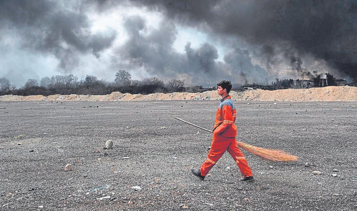 Un barrendero camina por delante del Depósito de Petróleo de Teherán, atacado por Israel.