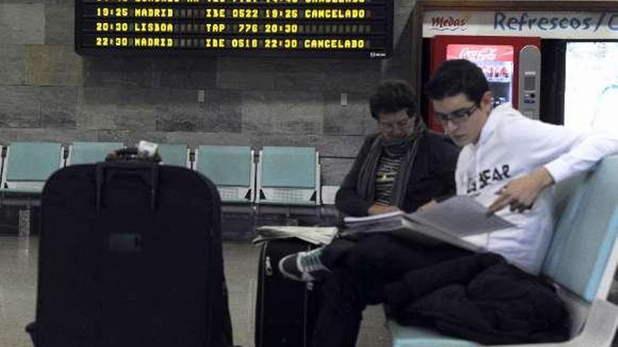 Dos pasajeros esperan en la terminal de Alvedro. / juan varela