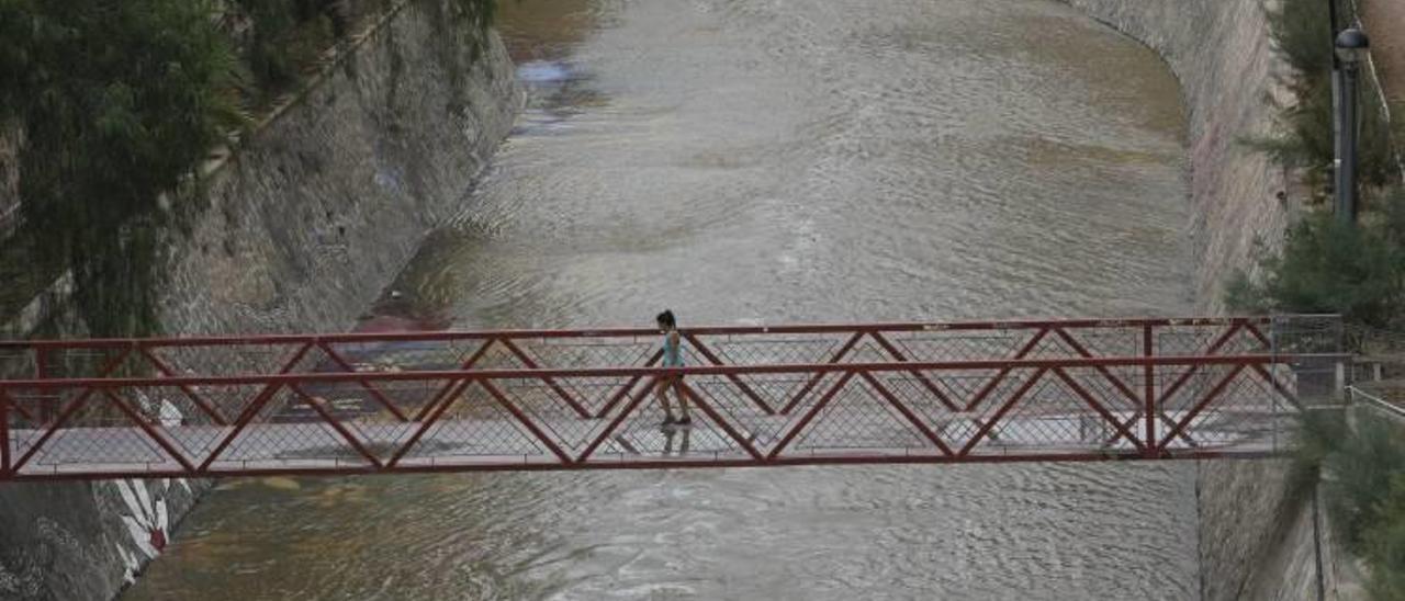 Una mujer cruza por una pasarela sobre un cauce repleto de agua.