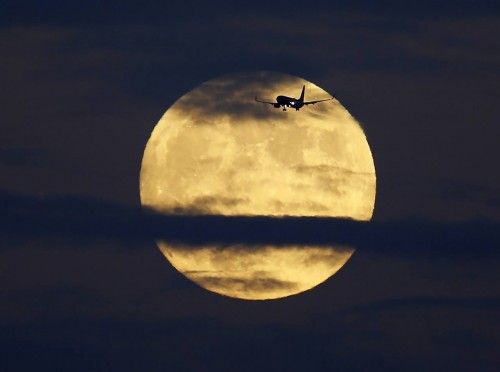 A commercial airliner crosses the path of a rising full moon as it comes in to land at Lindberg Field in San Diego, California