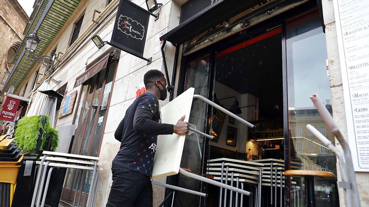 Un trabajador recoge mesas en un bar del centro de València por el cierre de la hostelería a media tarde.