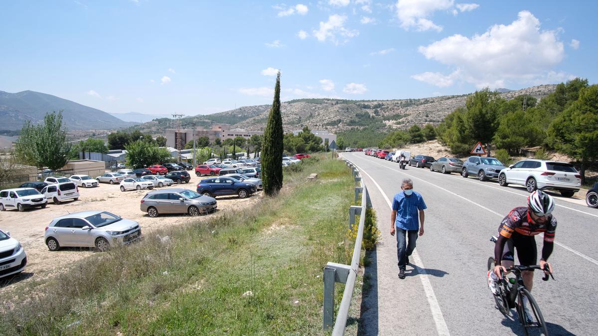 Coches en los arcenes de la carretera, a la izquierda el solar de Asprodis donde está prohibido estacionar y al fondo el Hospital de Elda.