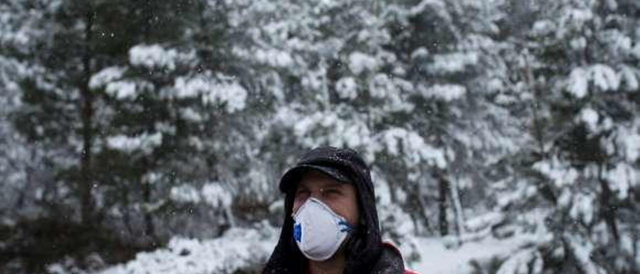 Un hombre con mascarilla bajo la nieve, ayer en Riós. // EFE / Brais L.