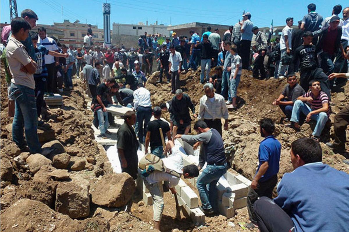 Habitants de Hula (Síria) col·loquen lloses sobre una fossa comuna per a les víctimes d’un bombardeig en una zona residencial de la ciutat. Almenys, 108 persones han mort en l’atac.