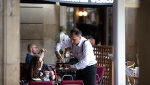Un camarero atiende a un cliente en la terraza de un bar.