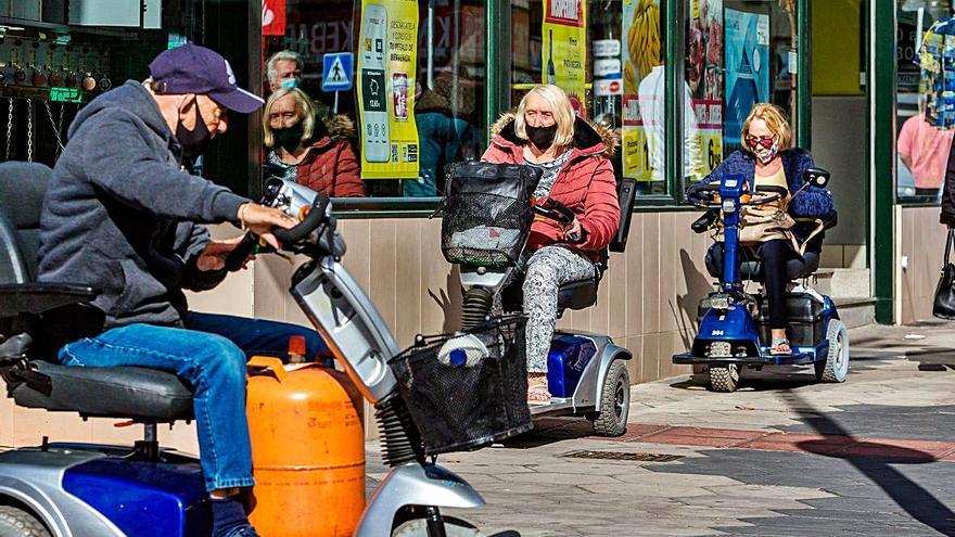 Un grupo de británicos con sillas eléctricas en una de las calles del Rincón de Loix. A la derecha, comercios ingleses en Benidorm. | DAVID REVENGA