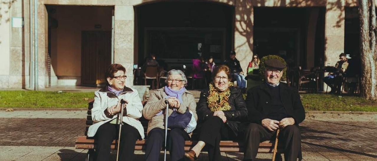 Parroquianos en la plaza Mayor de Llaranes tomando el sol en un banco.