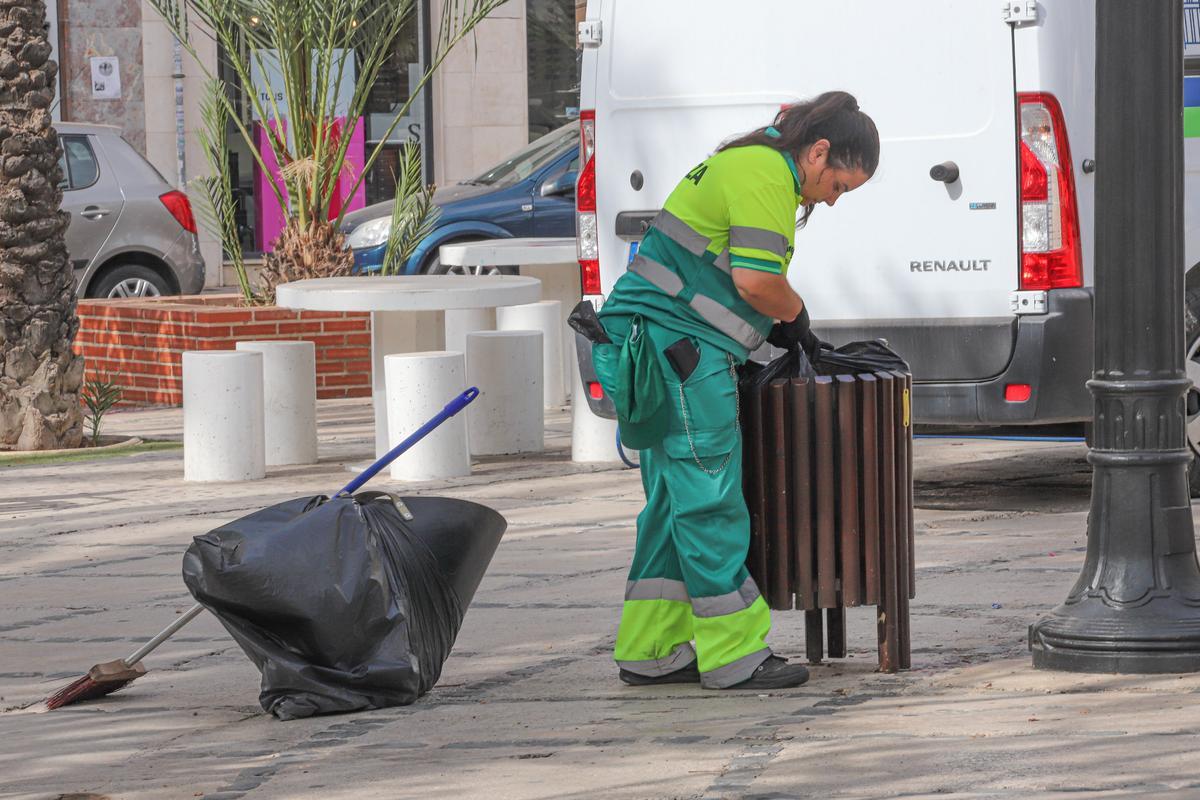Una trabajadora vacía una papelera en el jardín de la Plaza de Madrid, en Elche