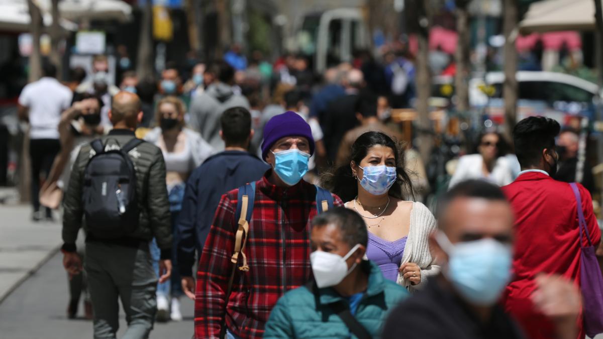 Multitud de personas pasean por la calle con mascarilla.