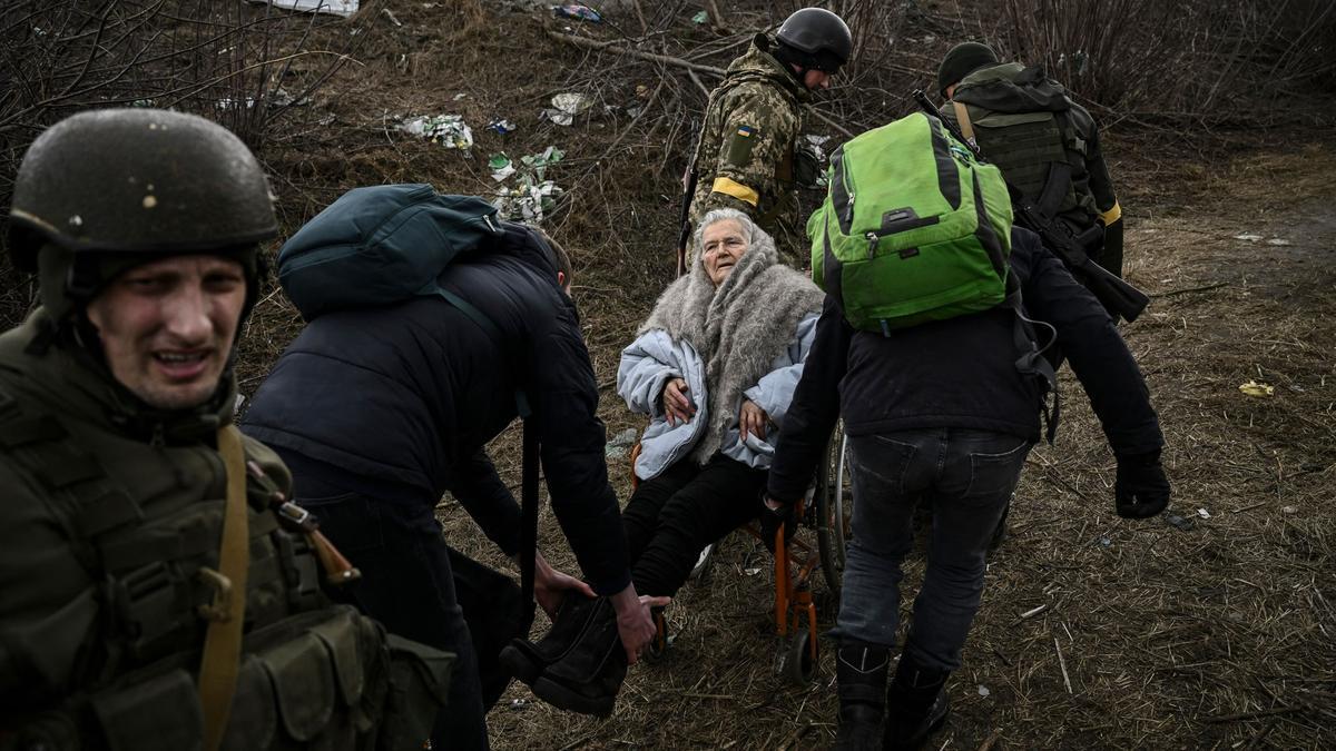 Un grupo de personas ayudan a una anciana en silla de ruedas mientras evacuan la ciudad de Irpin, al oeste de Kiev, el 7 de marzo de 2022.