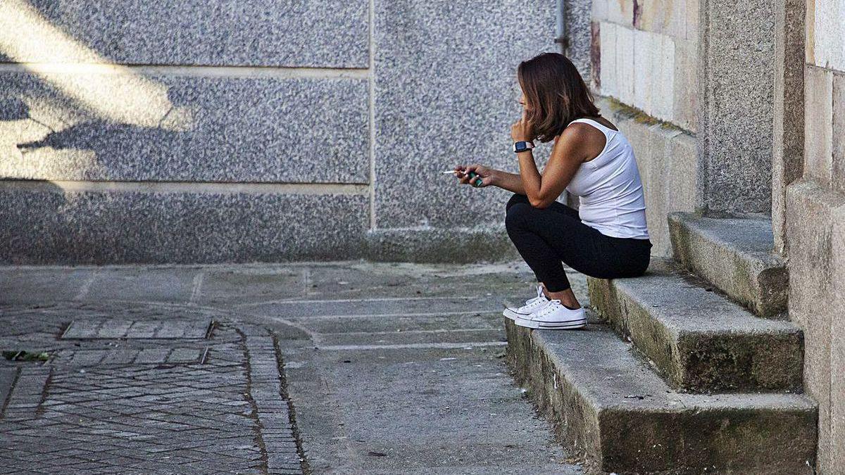 Uma mujer se fuma un cigarrillo sentada en unas escaleras, al aire libre.