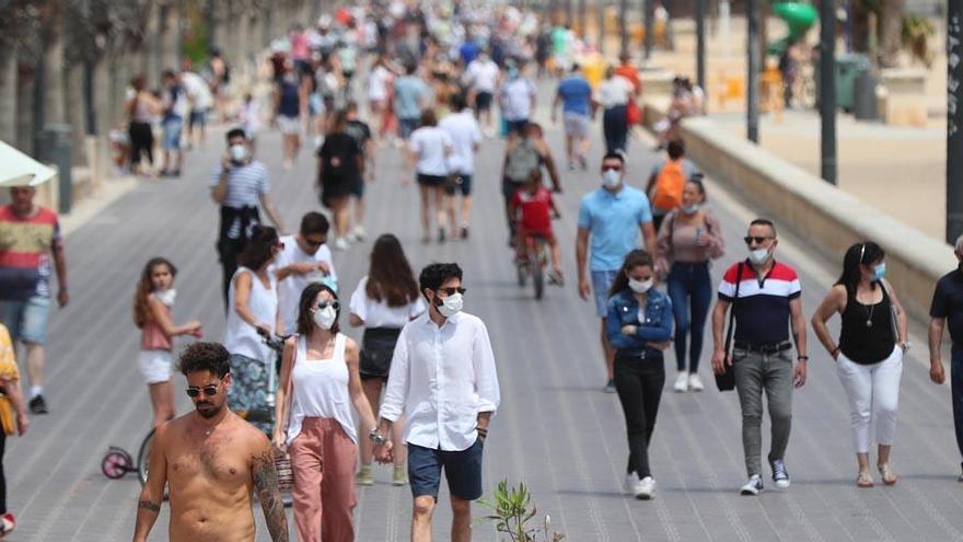 Decenas de personas caminan por el paseo marítimo de una playa de Valencia.