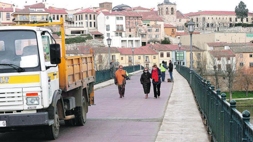 Varios peatones pasean por el Puente de Piedra mientras varios operarios inician las obras en el viaducto.
