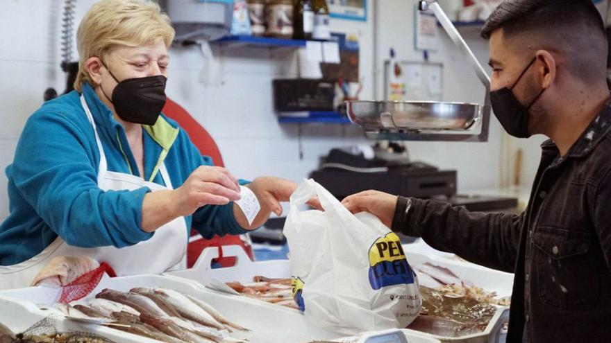 Una pescadera entrega un ticket de compra a un cliente.