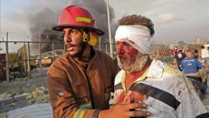 Un hombre herido es ayudado por un bombero, tras la explosión en el puerto de Beirut.