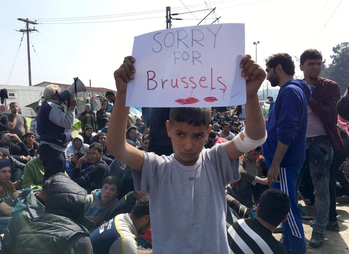 A refugee boy holds up placard reading Sorry for Brussels as refugees and migrants take part in a protest against the closure of the border at Greek-Macedonian