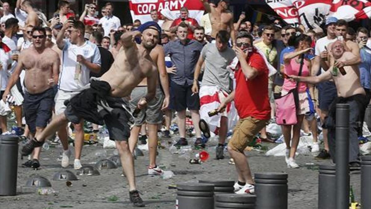 Decenas de 'hooligans' lanzan botellas y sillas contra aficionados rusos. La policía francesa (izquierda) detiene a un seguidor, ayer durante los enfrentamientos en el puerto viejo de Marsella, antes del partido entre Inglaterra y Rusia.