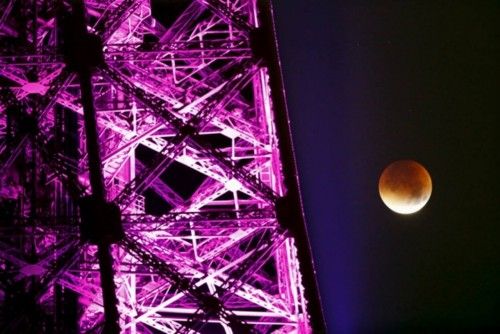 The Moon, appearing next to the Eiffel Tower in a dim red colour, is covered by the Earth's shadow during a total lunar eclipse over Paris