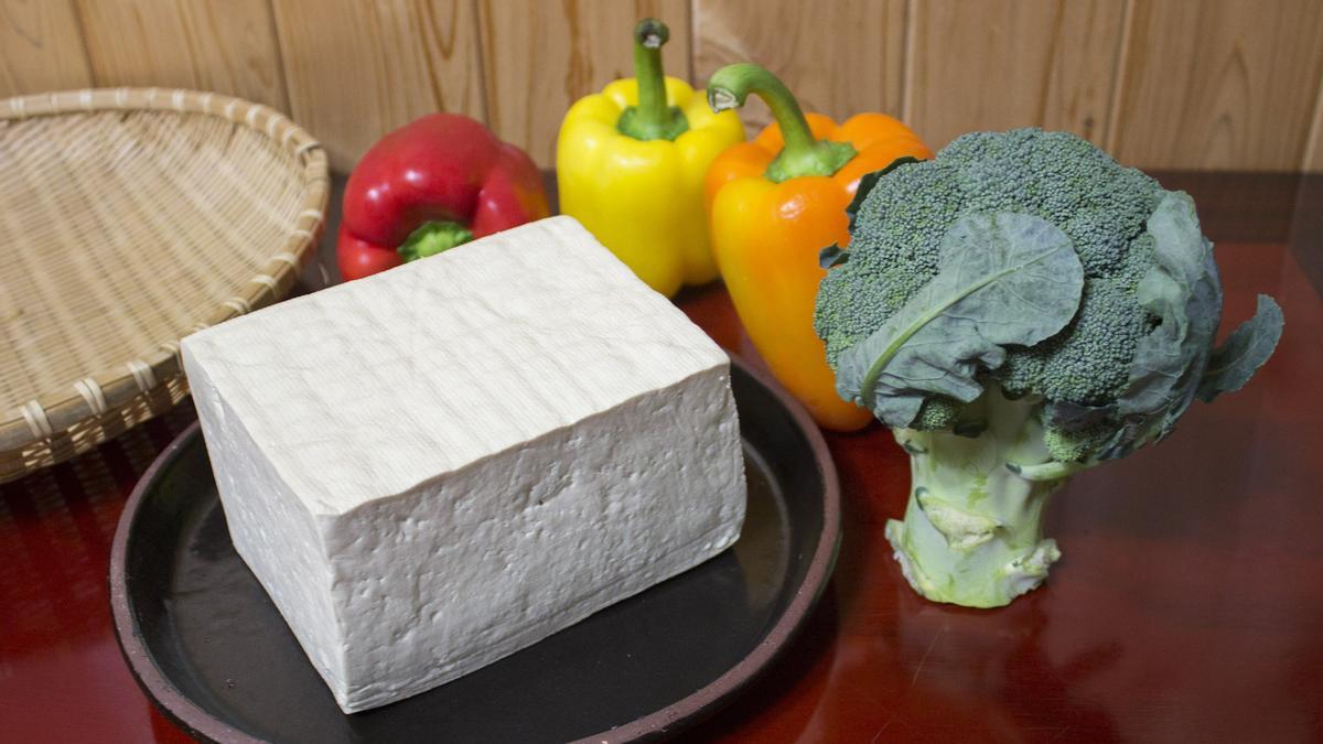 Un bloque de tofu, junto a unos pimientos y un tronco de brócoli.