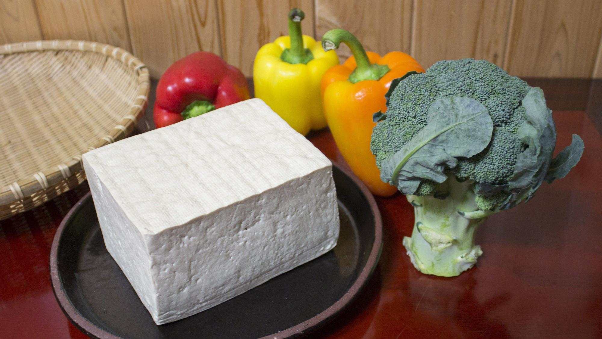 Un bloque de tofu, junto a unos pimientos y un tronco de brócoli