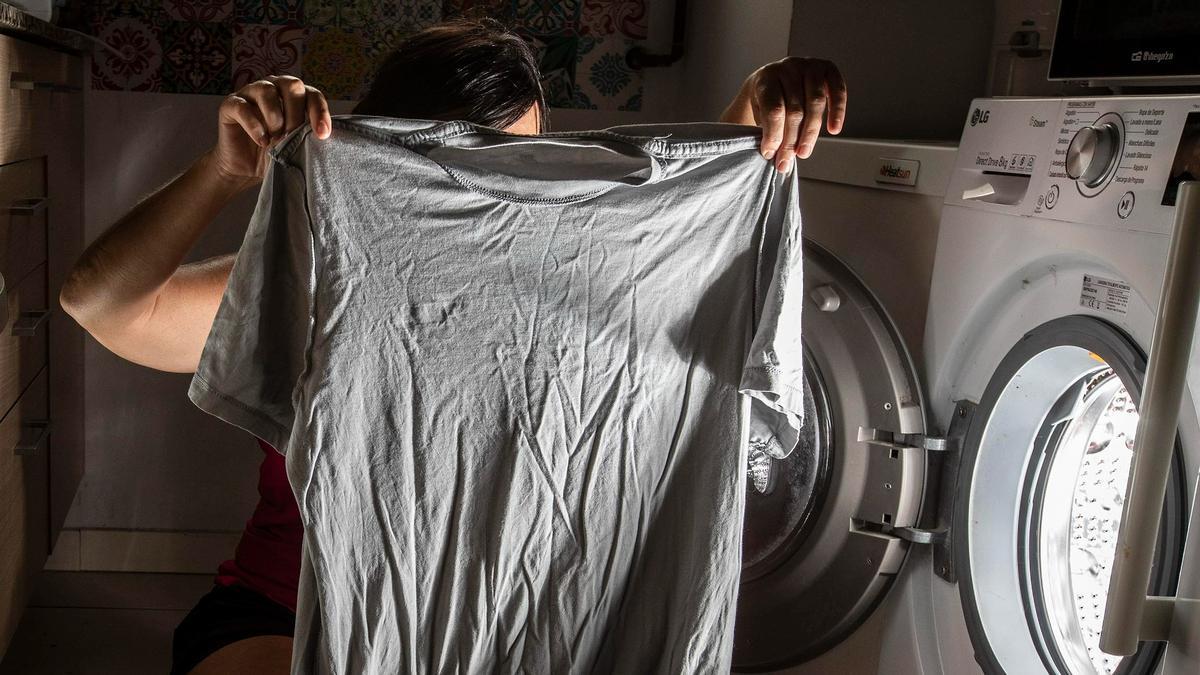 Una mujer muestra una camiseta que va a poner en la lavadora.