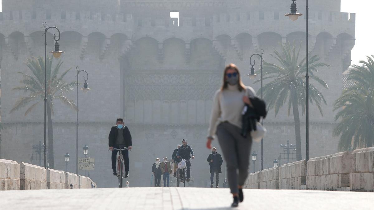 Varias personas cruzan el puente frente a las Torres de Serranos protegidas con mascarillas.