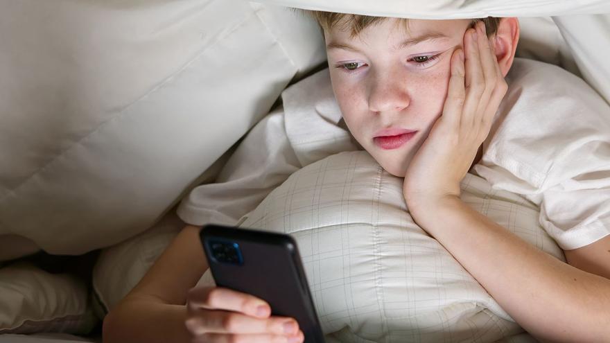 Un niño juega con el teléfono móvil antes de irse a dormir.
