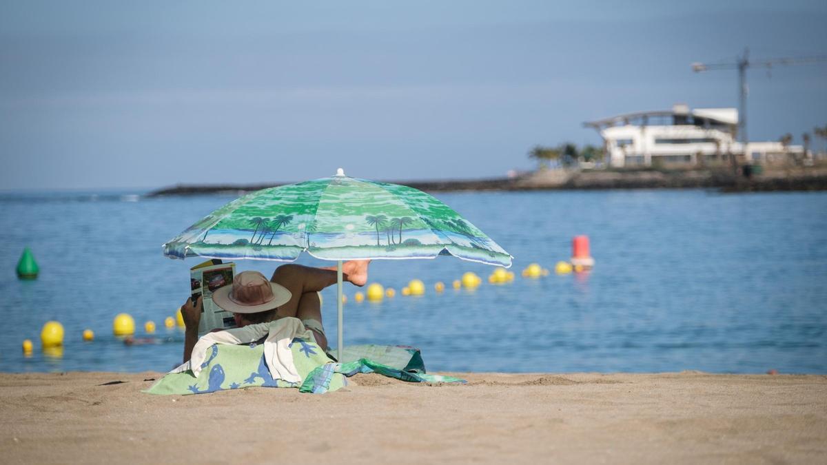 Un turista lee una revista bajo la sombrilla en una playa de las Islas.