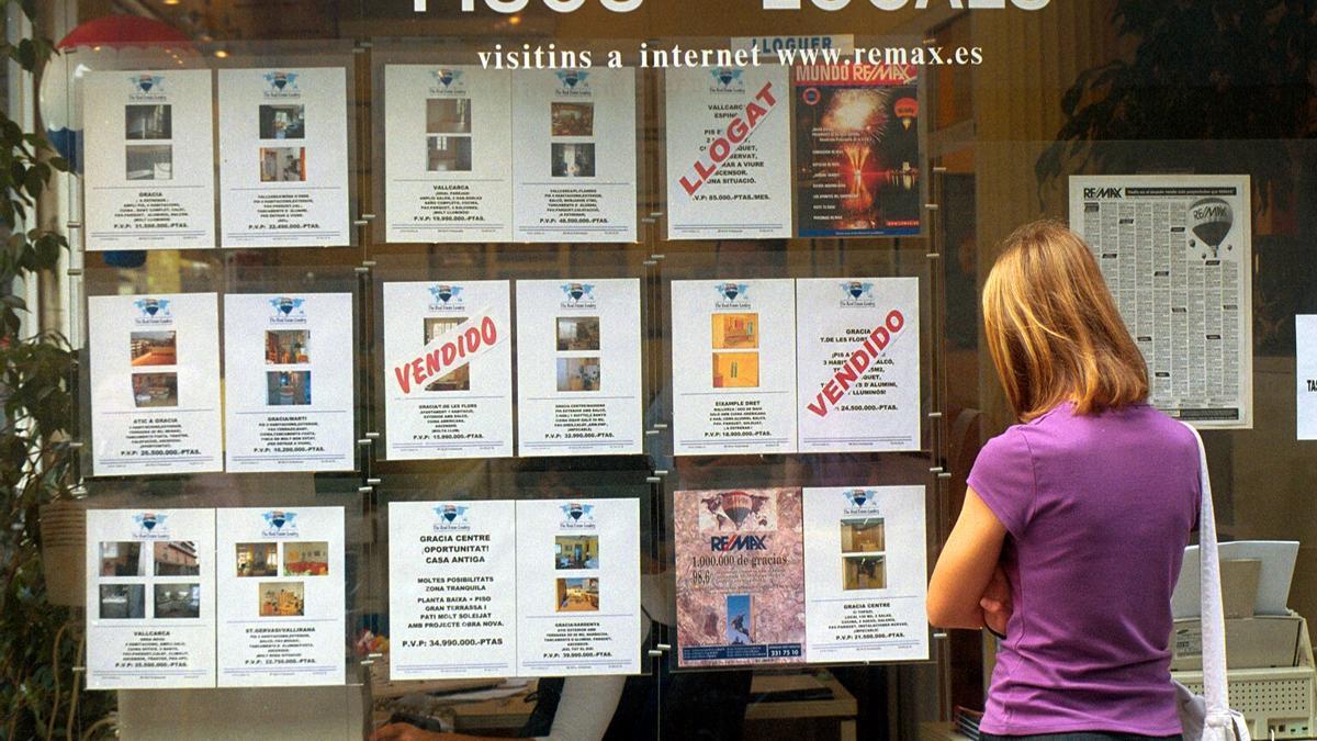 Una mujer observa los anuncios de pisos del escaparate de una agencia inmobiliaria en Barcelona.