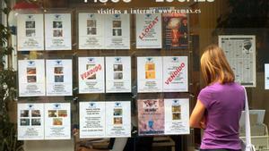 Una mujer observa los anuncios de pisos del escaparate de una agencia inmobiliaria en Barcelona.