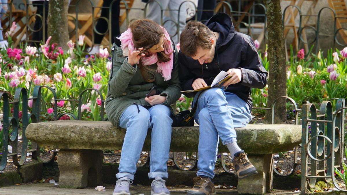 Una pareja de turistas sentados en un banco en la Praza de Fonseca