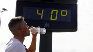 Un joven bebe agua junto a un termómetro que marca 40 grados.