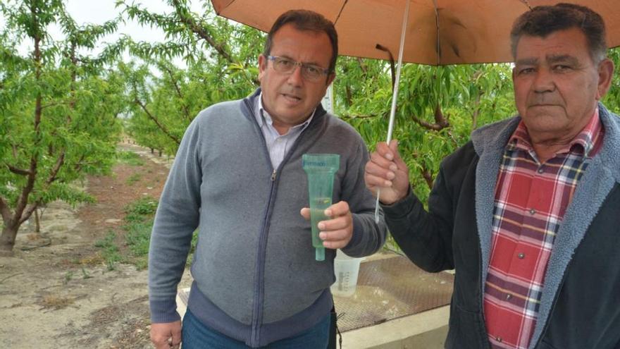 Manuel Martínez, de Coag Cieza, a la izqda., muestra un pluviómetro con las lluvia caída.