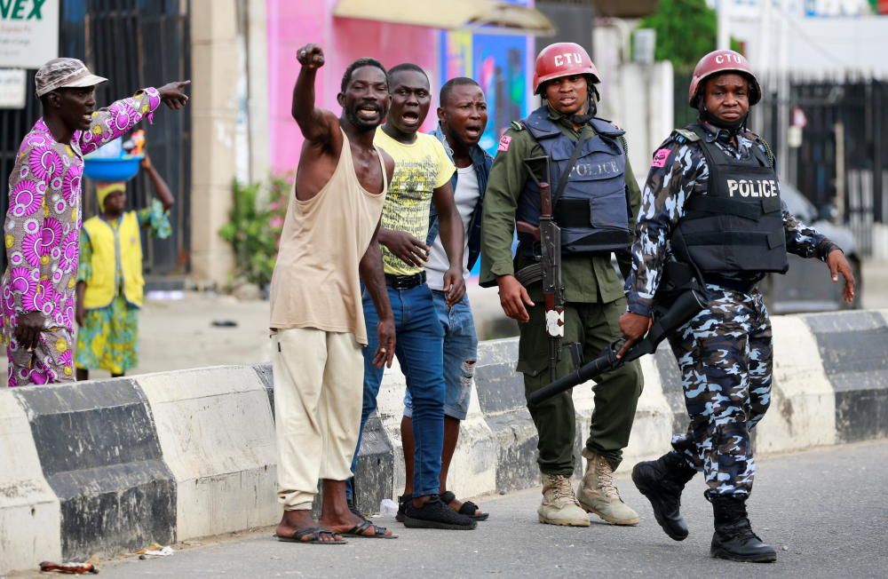 Men gesture as they stand near police officers ...